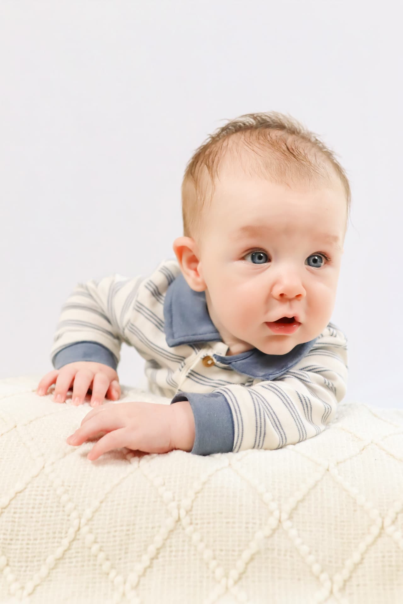Close-up studio portrait of a baby in a striped polo shirt during tummy time