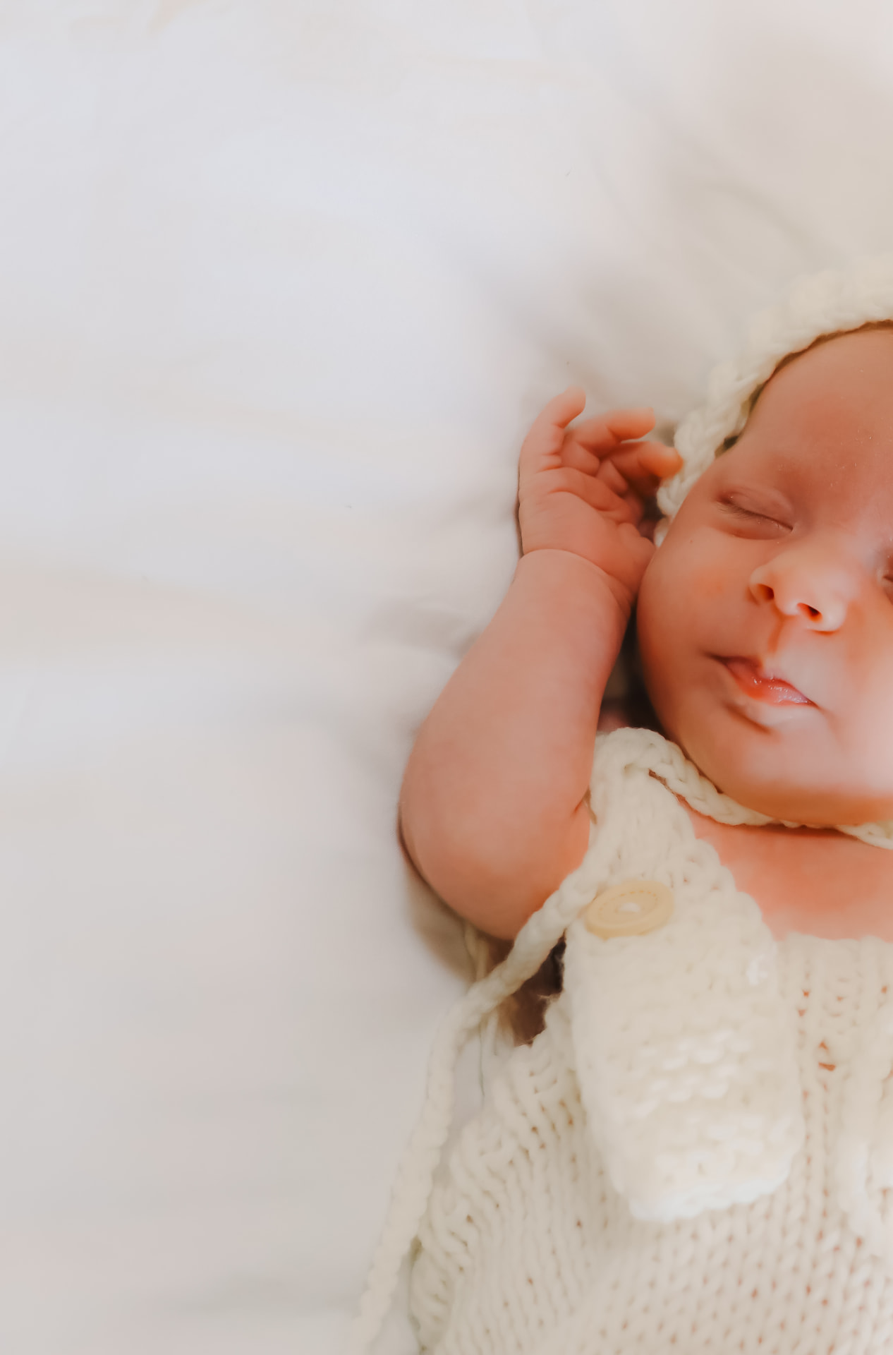 A peaceful newborn sleeping in a soft cream knitted outfit and bonnet