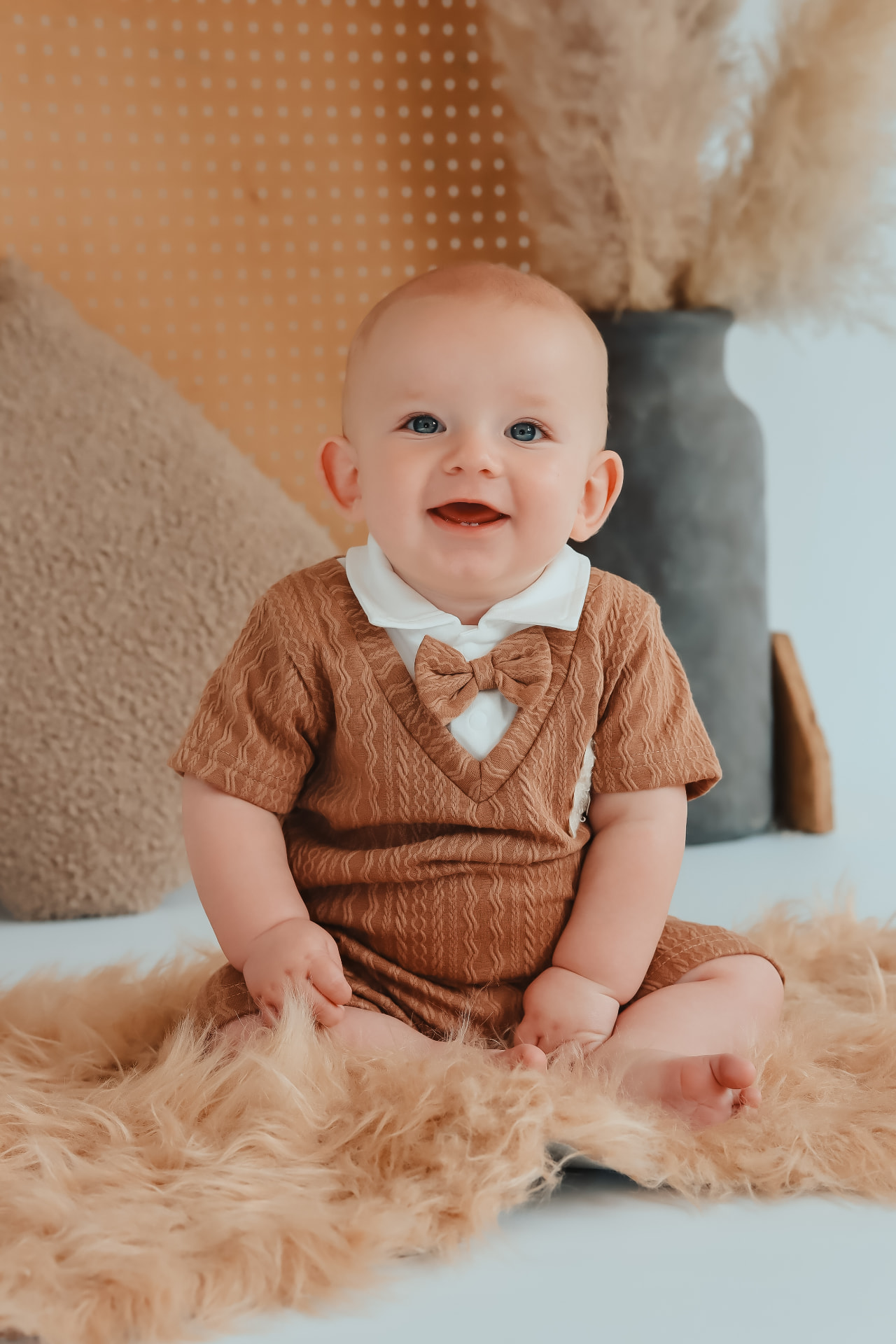 Smiling baby boy in a knitted bow tie outfit on a sheepskin rug