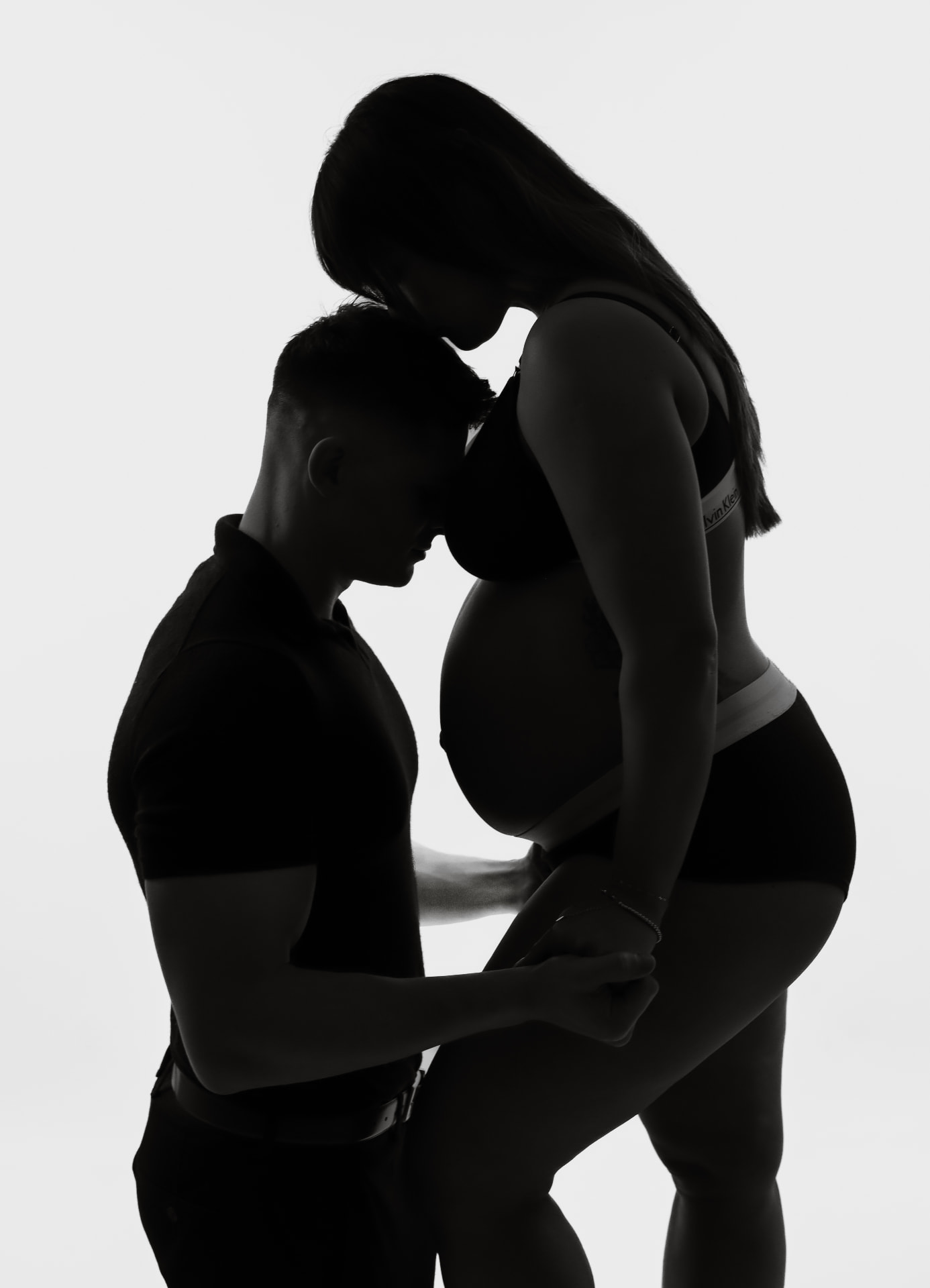 Backlit silhouette of an expectant mother with her partner resting against the bump