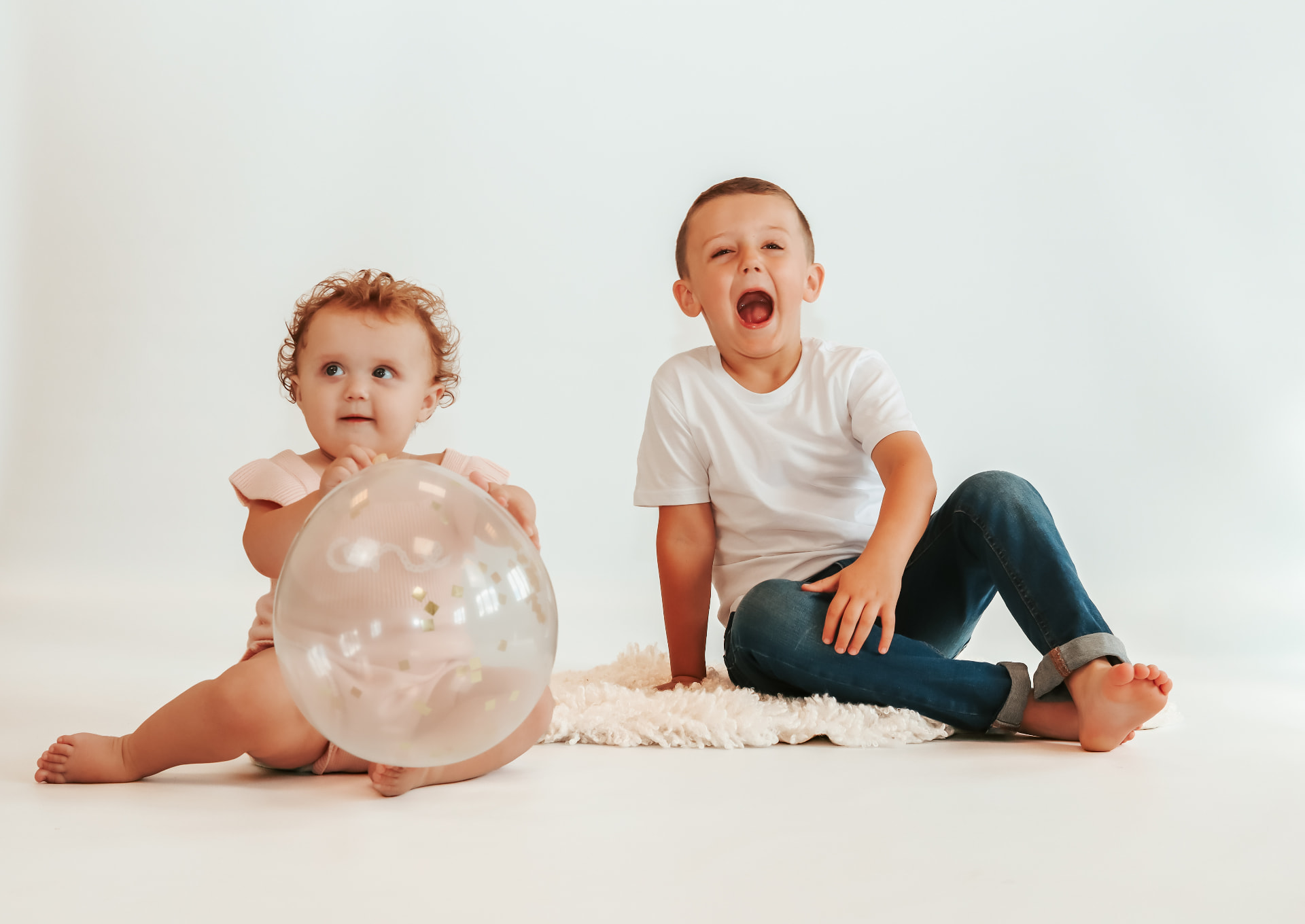 Little girl holding a confetti balloon beside her laughing big brother in the studio