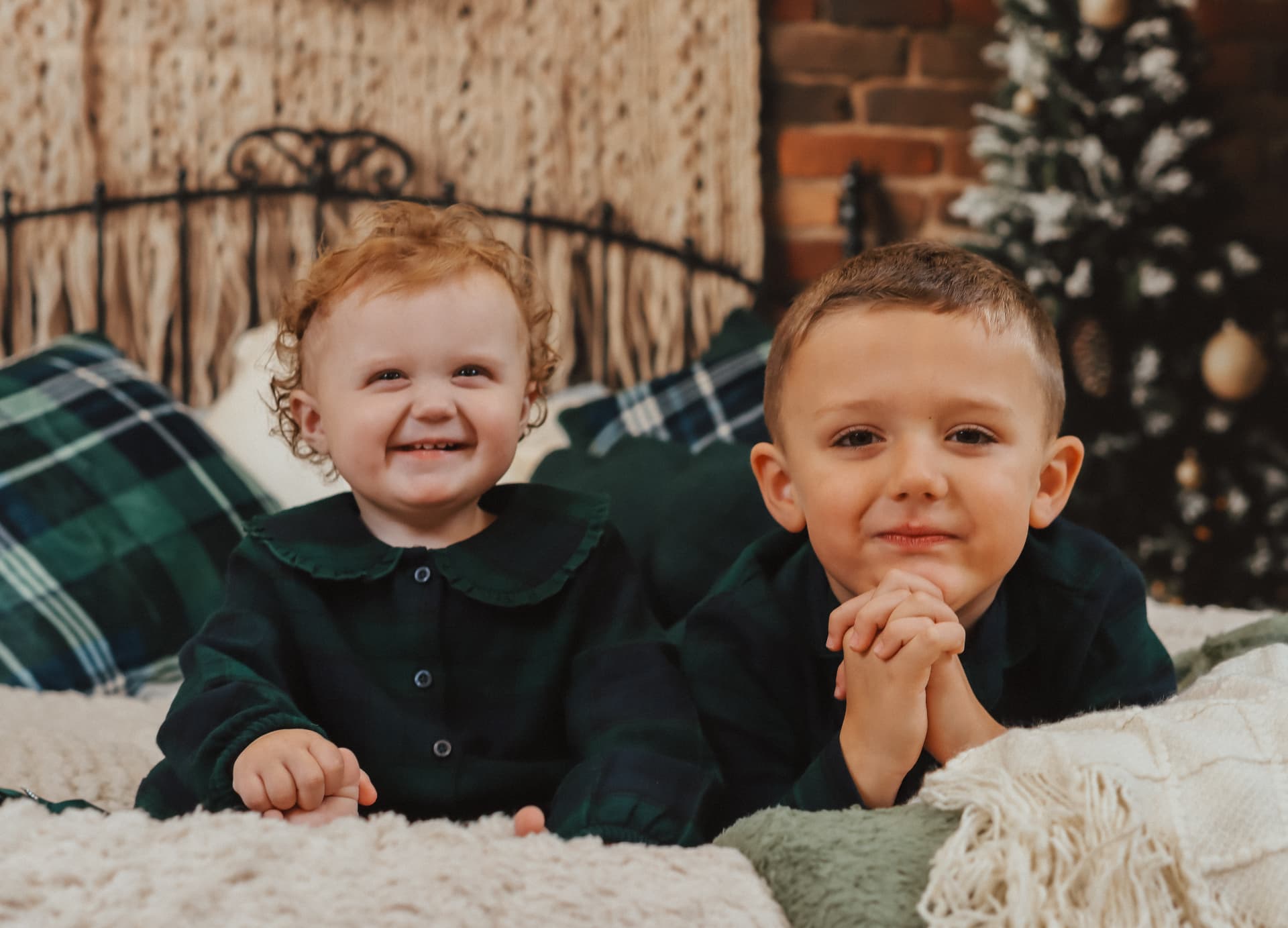 Brother and sister in tartan pyjamas smiling on a Christmas bed