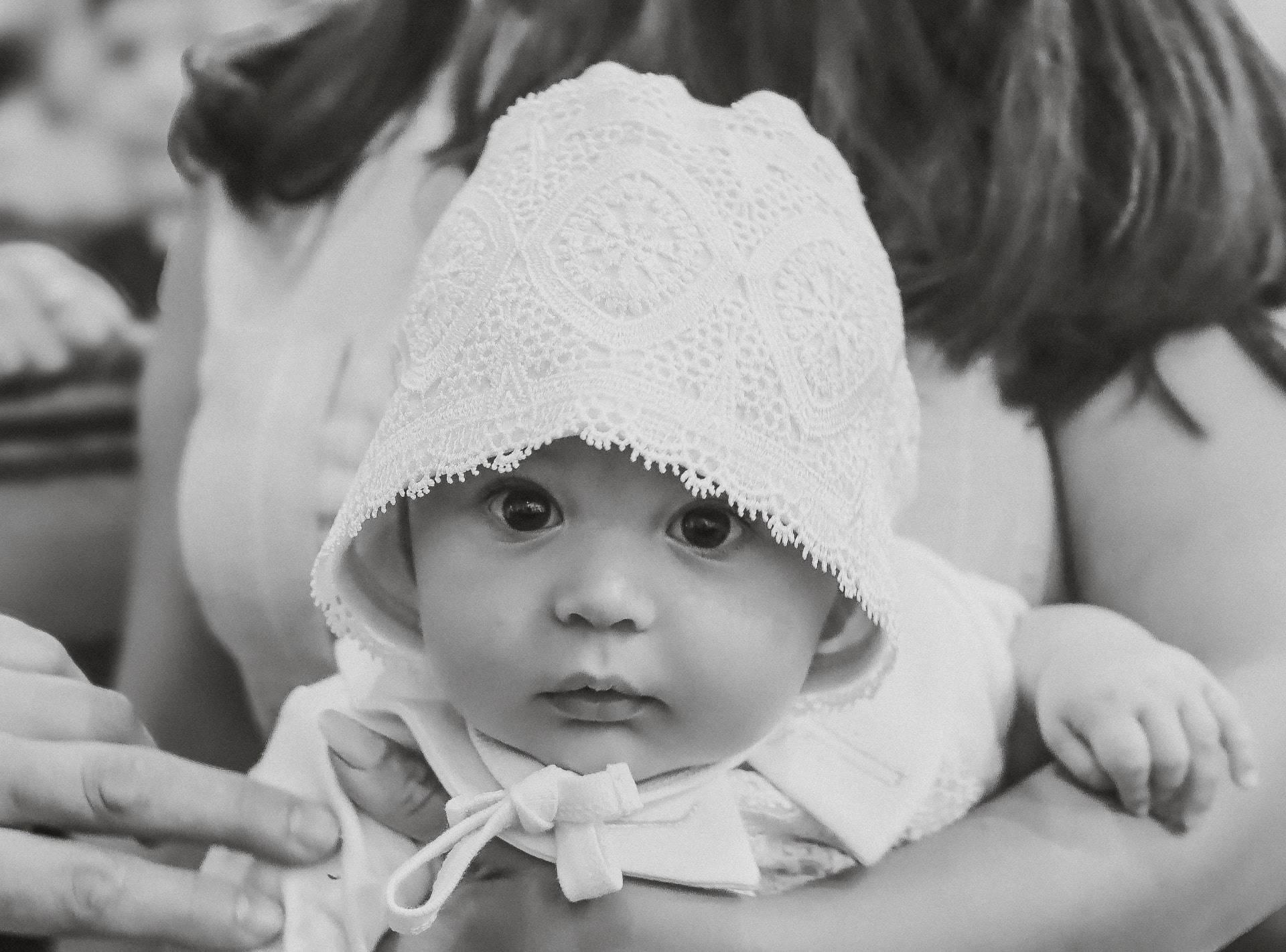 Black and white photograph of a baby in a lace christening bonnet held by family