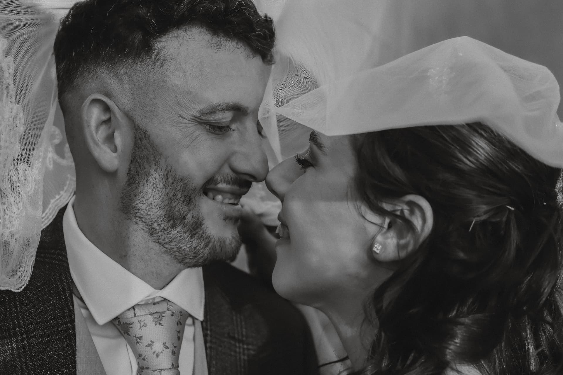 Black and white intimate portrait of bride and groom almost kissing beneath a lace veil