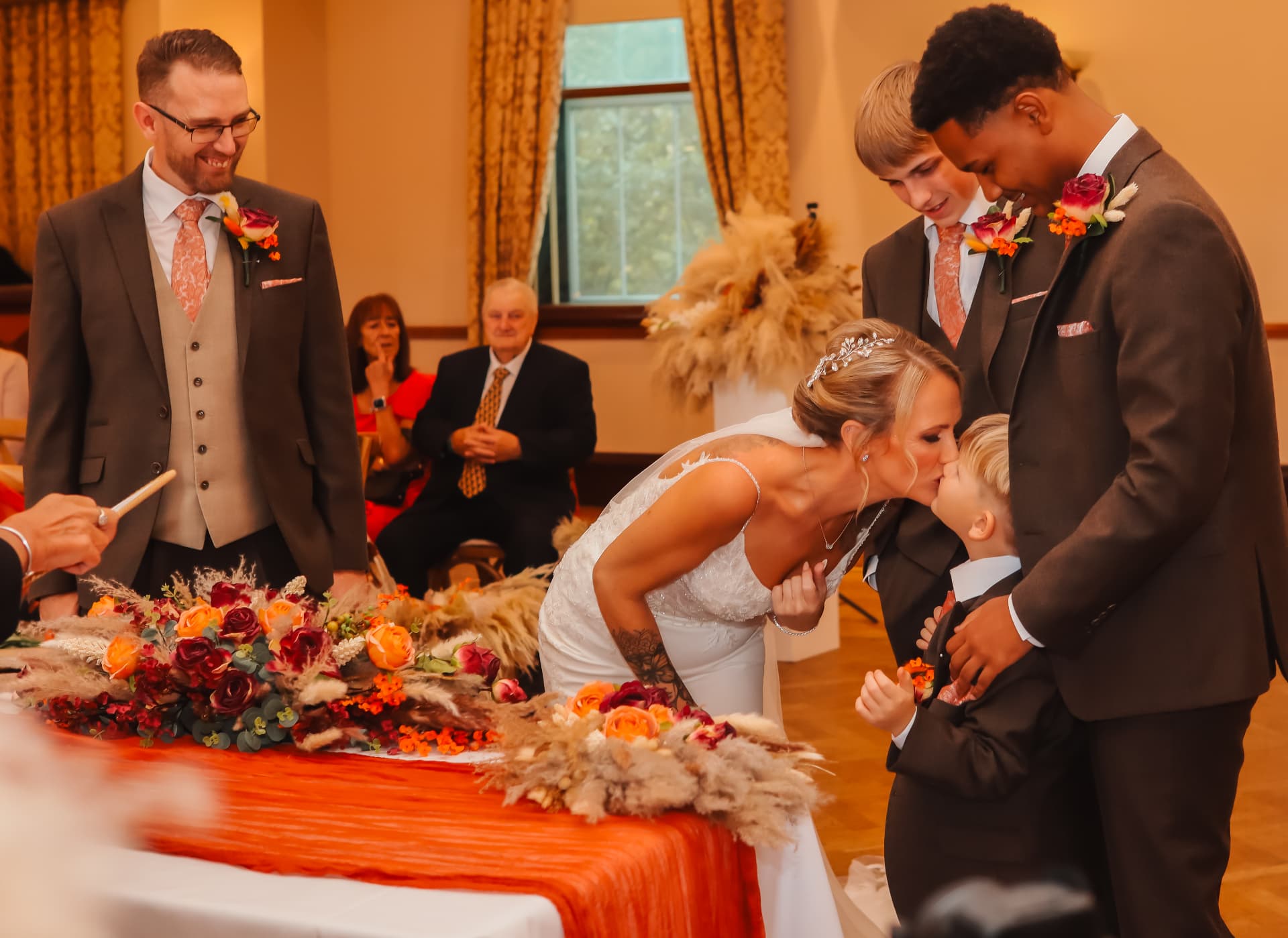 Bride kissing her young son during the ceremony surrounded by autumn flowers