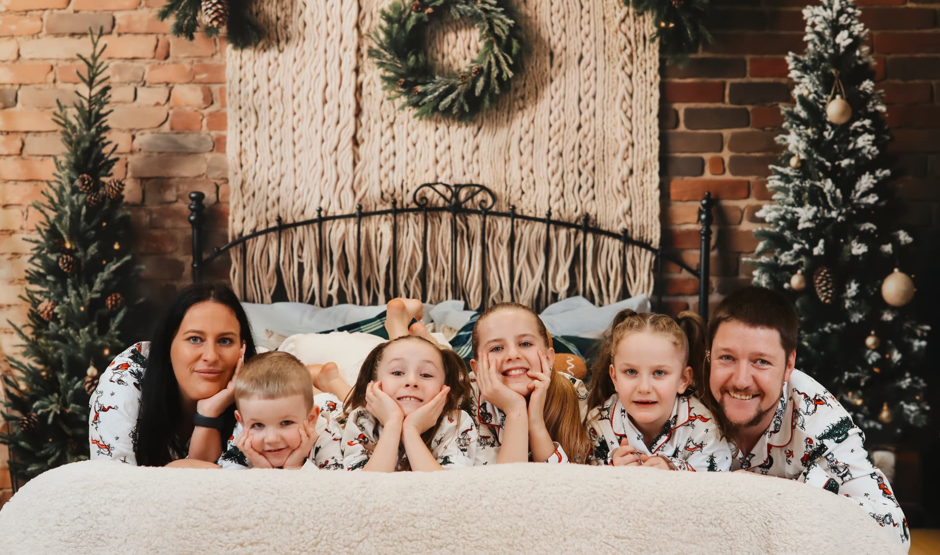 Large family in matching Christmas pyjamas lying on a bed between two decorated trees