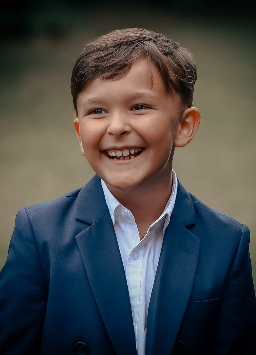 Young boy in a navy suit laughing outdoors
