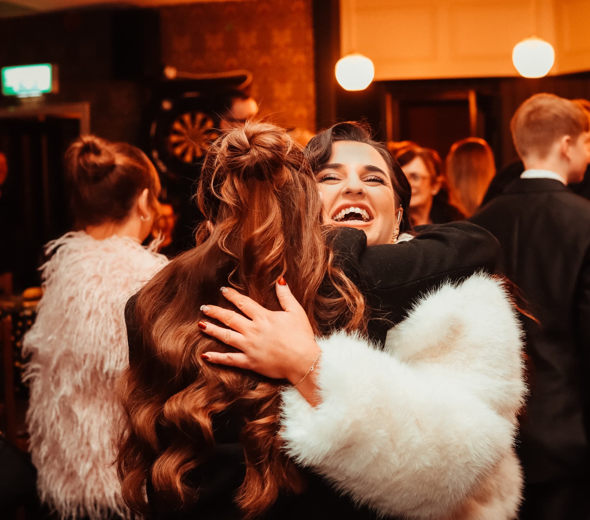 Two guests laughing mid-hug at an evening celebration
