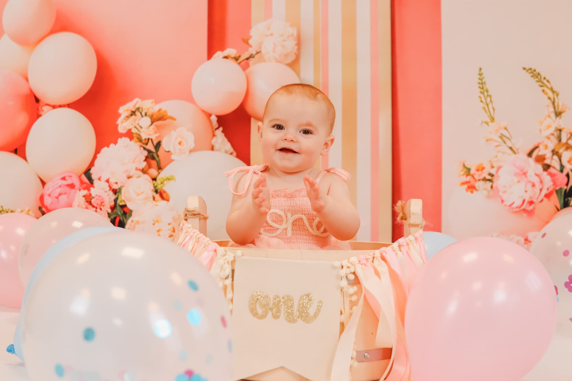 Baby girl clapping in a decorated crate at her first birthday cake smash